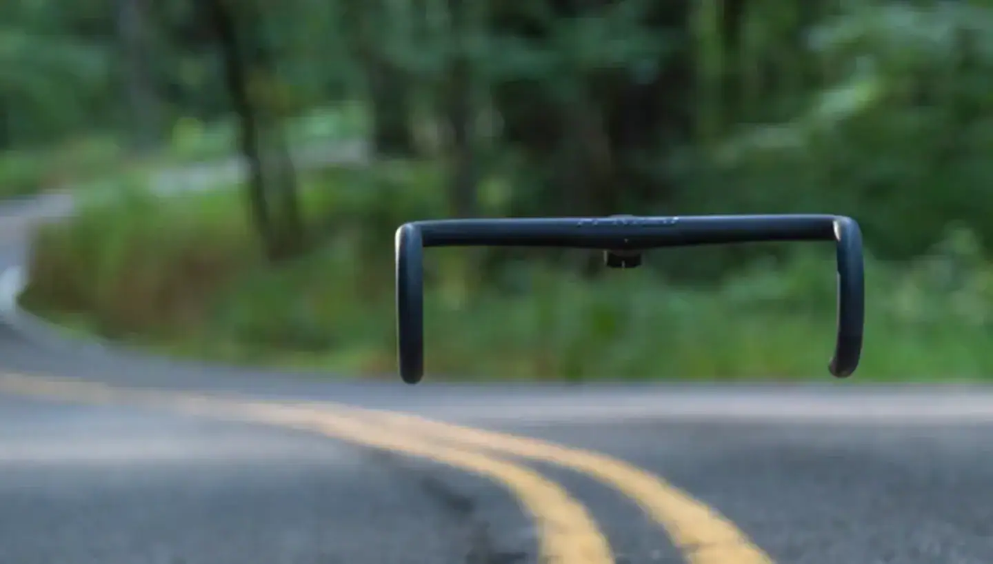 Road safety barrier on a rural road with double yellow lines, surrounded by lush green trees and blurred background, representing traffic control and infrastructure.